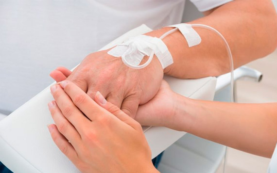 Fotografía de un brazo con un tratamiento intravenoso, sostenido por otra mano